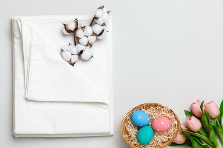 Top view of a stack of white bedsheets sets, cotton branch and a basket with Easter eggs. Copy space.の写真素材