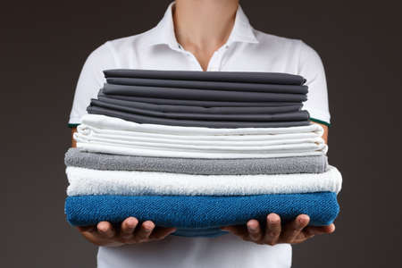 Close-up of a woman holding a stack of clean rolled towels and bedsheets.の写真素材