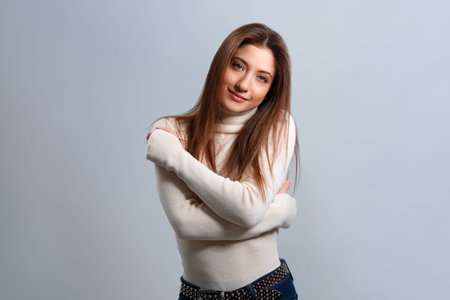 A beautiful smiling girl hugs herself with her hands. Portrait of a young woman in a soft sweater...