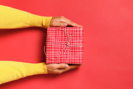 Close-up of female hands holding a gift box on a red background. Birthday valentine's day new year christmas.の写真素材