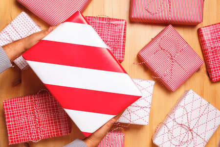 Close-up of male hands are holding a Christmas box with a present on the background of many gifts. Top view.の写真素材