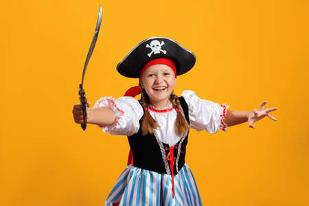 Halloween celebration. Cheerful girl in a carnival costume of a pirate in the studio on a colored yellow background.の写真素材