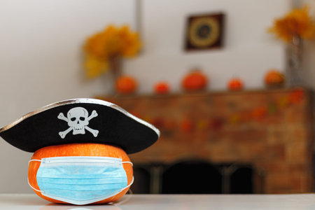 Halloween pumpkin with a pirate hat in a protective mask on the table against the background of a home fireplace with autumn decorations.の写真素材