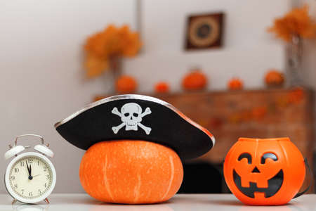 Halloween pumpkin with pirate hat, bucket jack-o-lantern and alarm clock on the table against the background of a home fireplace with autumn decorations.の写真素材