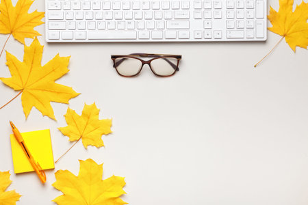 Top view of a white work desk with a keyboard, glasses, autumn maple leaves. Flat lay copy spaceの写真素材