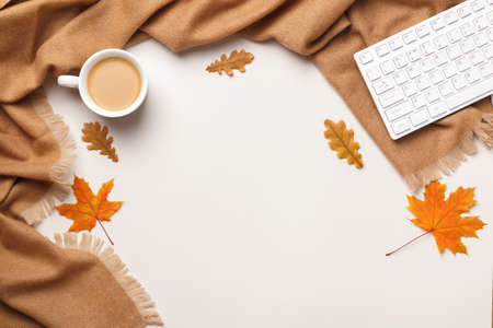 Autumn workplace coziness composition concept. Cashmere scarf keyboard coffee cup with autumn maple and oak leaves on a light gray background. Flat lay top view copy spaceの写真素材