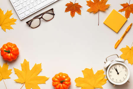 Top view of desktop with keyboard glasses note paper alarm clock with autumn leaves and pumpkins. Flat lay copy spaceの写真素材