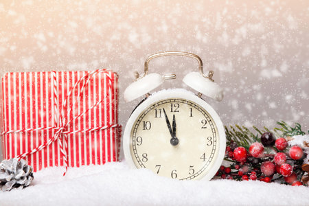 Alarm clock and Christmas gift with a fir branch in the snow.