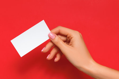 Female hand holding blank card on isolated red backgroundの写真素材