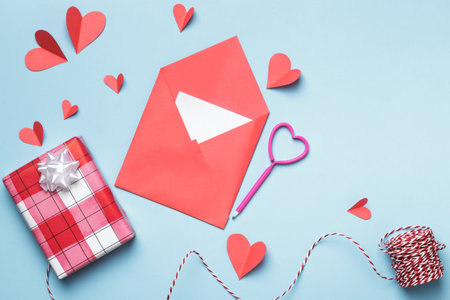 Love letter Valentine day concept. Red paper envelope with a white note inside and paper hearts a gift on a blue background.の写真素材