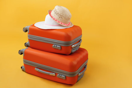 Two lying suitcases of travel bags and straw hats on a yellow background with copy space. The concept of summer time, vacation, tourism.の写真素材