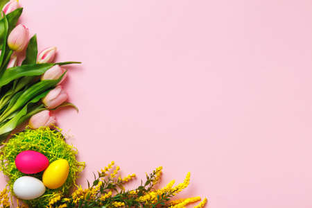 Top view of easter eggs and tulip flower sprigs on pink background with copy spaceの写真素材