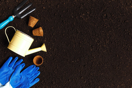 Garden tools on the soil. Fork watering can gloves