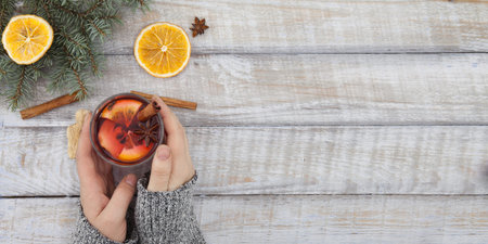 Christmas background, mulled wine in women's hands on a wooden table, top view