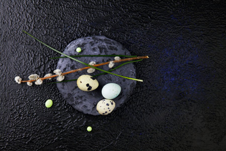 Easter eggs and pussy willow branches standing on a round slate stone on a dark textured background...