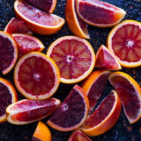 Slices, slices and wedges of red orange on a dark textured backgroundの写真素材