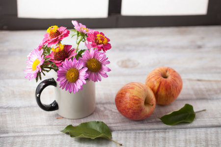 Still life with apples and flowers on a wooden surface by the windowの写真素材