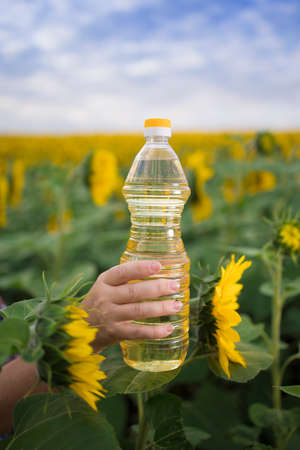 A hand with a bottle of golden sunflower oil raised up against the background of a field of blooming sunflowers in a sunny copy spaceの写真素材