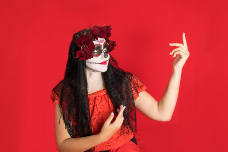 Portrait of a young woman in a red dress and traditional sugar skull makeup for the celebration of...