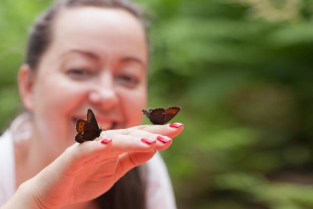 Portrait of an adult happy brunette woman holding butterflies in her hand in a forest clearing and showing psychological appeasementの写真素材