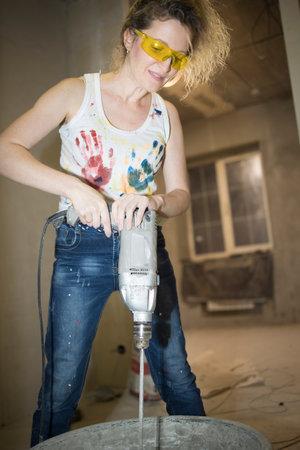 Young fair-haired curly woman makes repairs in the dwelling with construction toolsの写真素材