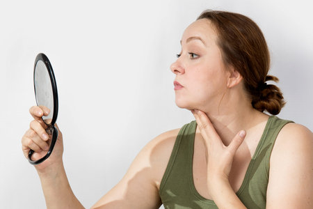 A middle-aged woman looks worriedly at herself in the mirror. High quality photo
