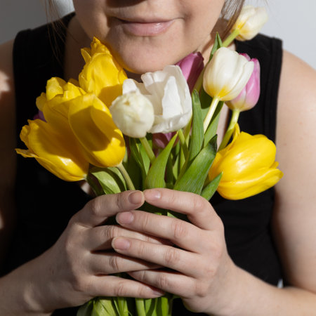 A woman smells colorful tulips in her hands in a room illuminated by sunlight. High quality photo