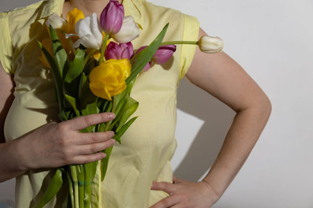 Multi-colored tulips in the hands of a woman in a room illuminated by sunlight. High quality photo