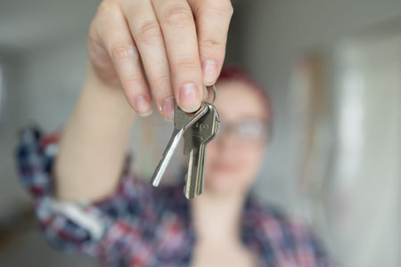 Woman holding keys in front of camera, background out of focus. High quality photo