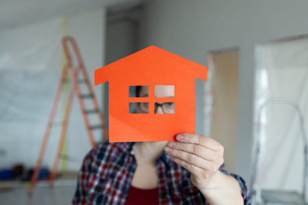 A person proudly holding an orange houseshaped cutout in their hands, symbolizing creativity in home renovationの写真素材