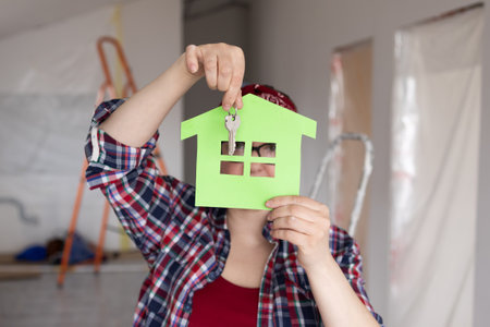 A person proudly showcasing a green house cutout while holding a key during their renovation projectの写真素材