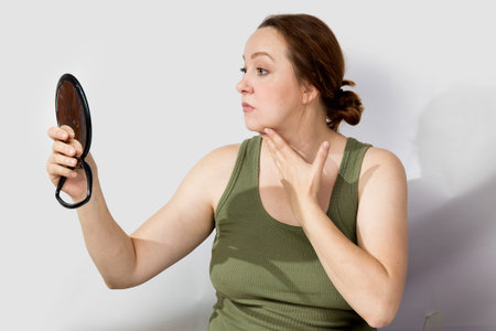 A middle-aged woman looks worriedly at herself in the mirror. High quality photo