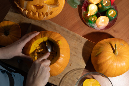 A person is enthusiastically scooping out a pumpkin for carving, surrounded by colorful festive decorationsの写真素材