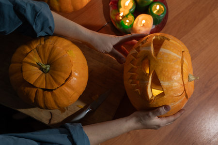 A creative person carves a spooky pumpkin for Halloween, lit by the warm glow of surrounding candlesの写真素材