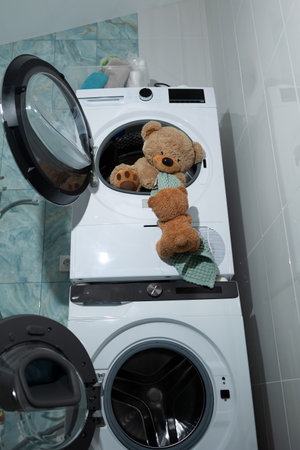 A playful teddy bear peeks out from a washing machine, capturing a whimsical and joyous laundry momentの写真素材