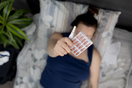 A person holds a medication blister pack while resting on a serene bed, emphasizing health awarenessの写真素材
