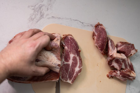 A skilled hand expertly slicing fresh pork meat on a robust wooden chopping board in a stylish...