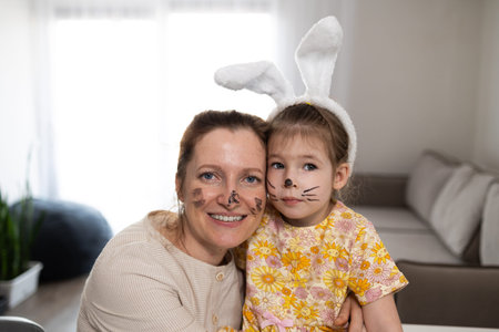 A joyous moment shared between a mother and her child, both wearing adorable bunny ears and face paint for Easterの写真素材