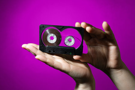 An engaging and visually appealing display of a vintage tape cassette held in hands against a vibrant purple backdropの写真素材