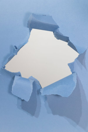A Yorkshire terrier playfully peeks through a torn section of light blue paper, showcasing its...
