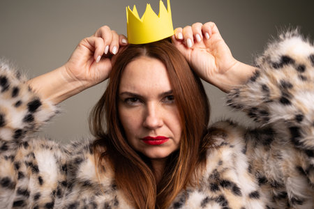 An angry and gloomy woman confidently poses in a leopard fur coat with a yellow crown, embodying strength and styleの写真素材