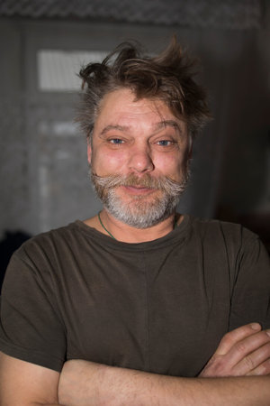 A man with a beard and mustache is standing with his arms crossed, showing off his facial hair. He...