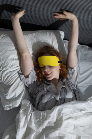 A woman stretches in bed with a charming yellow eye mask, embodying a moment of pure relaxation and...