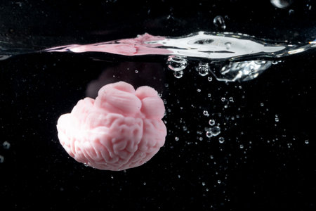 A pink brain floats just beneath the waters surface, creating splashes of water droplets around it....