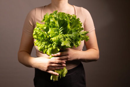 A person stands still, holding a large, fresh bunch of lettuce close to their chest. The background...