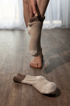 Warmth radiates from the underfloor heating as someone puts on cozy socks. The wooden floor offers a comfortable setting for relaxing feet. Soft light filters through a curtain.の写真素材