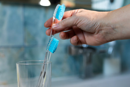 A hand places two new toothbrushes into a clear glass on a bathroom counter. It emphasizes regular replacement for dental and oral health. Copy space is present.の写真素材