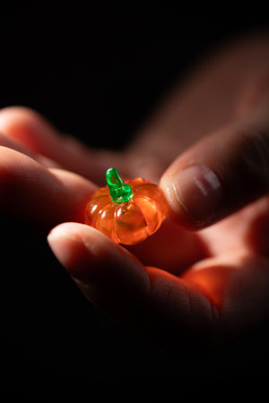 A person carefully holds a small, translucent orange pumpkin with a green stem in their hands. It could be used for an invitation to a Halloween party.の写真素材