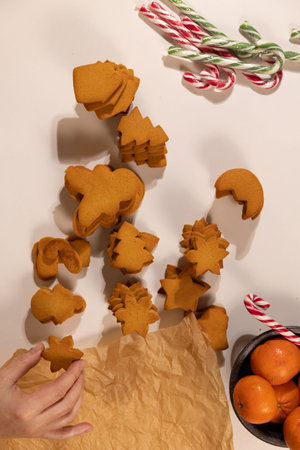 Hands are arranging various gingerbread cookie shapes like stars and trees on a table, preparing for...