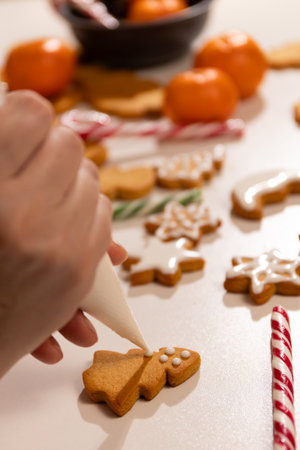 A cook decorates gingerbread cookies with icing during a joyful Christmas celebration. The scene includes vibrant tangerines and striped candy canes, enhancing the holiday spirit.の写真素材